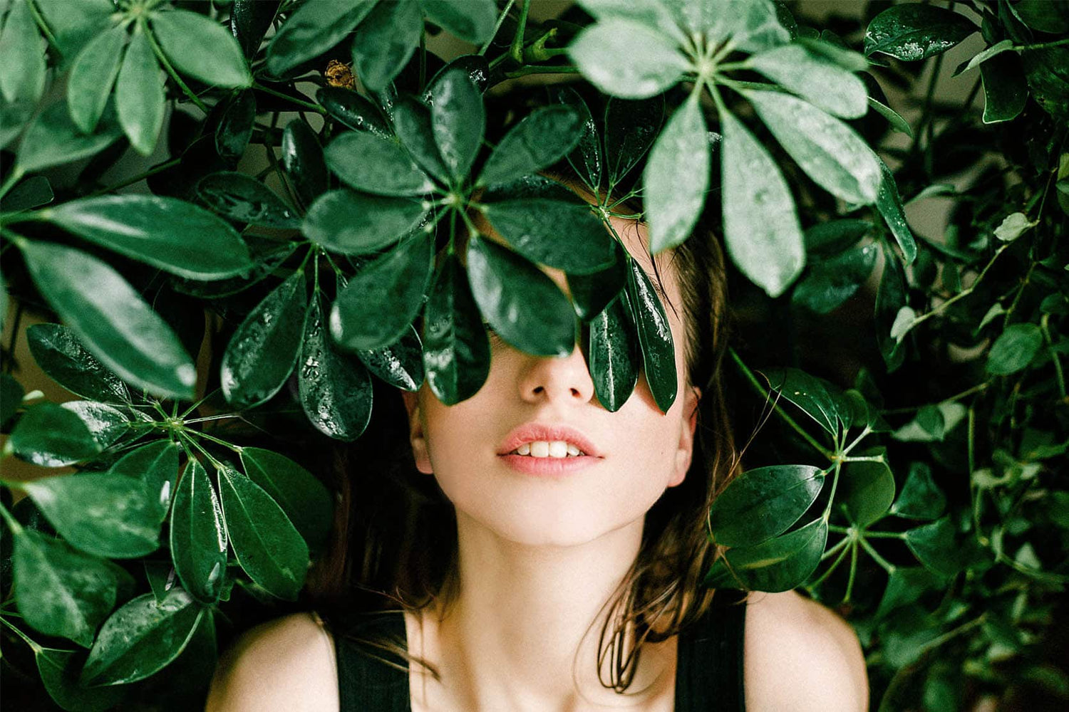 Woman lying in a bed of wet leaves slightly covering the top half of her face