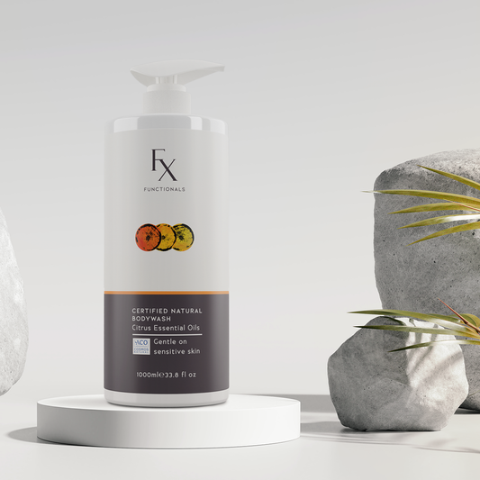 Functionals Certified Natural Bodywash with citrus essential oils on podium surrounded by rocks and palm fronds